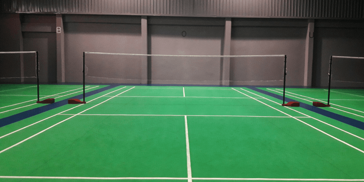 Indoor badminton court featuring green flooring and multiple nets set up