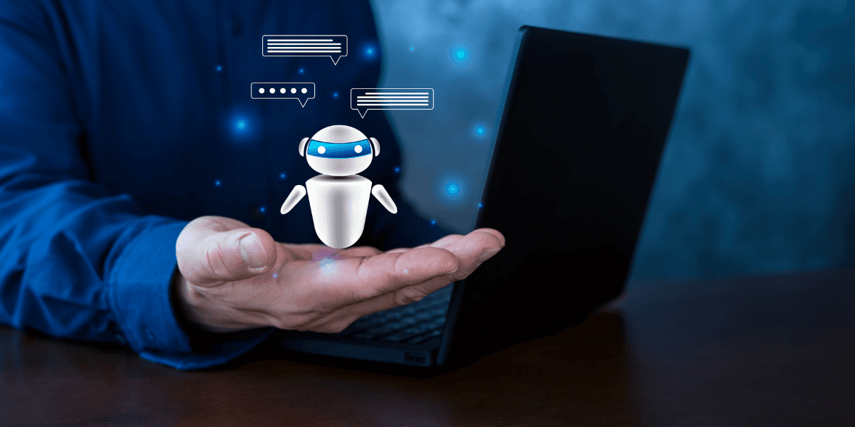 A person holding a small robot graphic above a laptop on a table