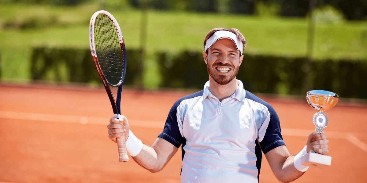 Smiling tennis player holding a trophy and racquet on a clay court