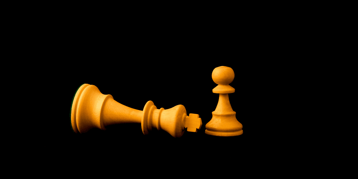 A fallen king chess piece next to a standing pawn on a black background
