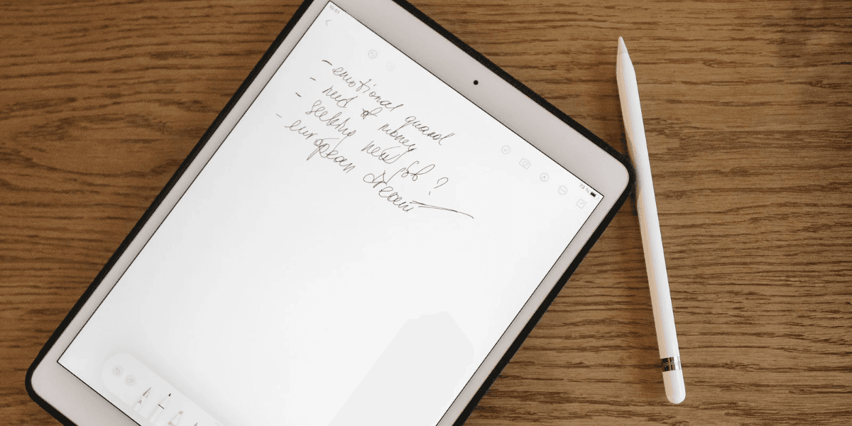 A tablet on a wooden surface displays handwritten notes beside a stylus.