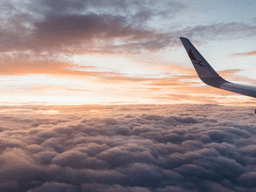 View from an airplane window above the clouds during sunrise with an aircraft wing visible.