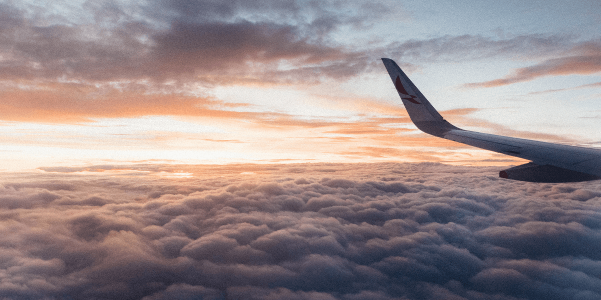 View from an airplane window above the clouds during sunrise with an aircraft wing visible.