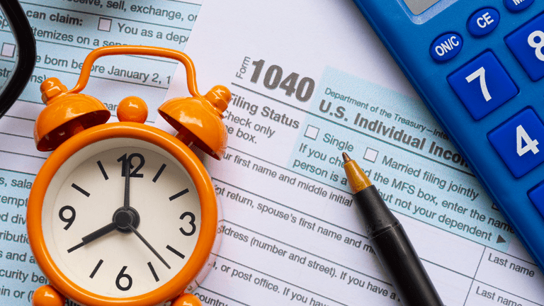 Tax form 1040 with a clock, calculator, and pen on a desk