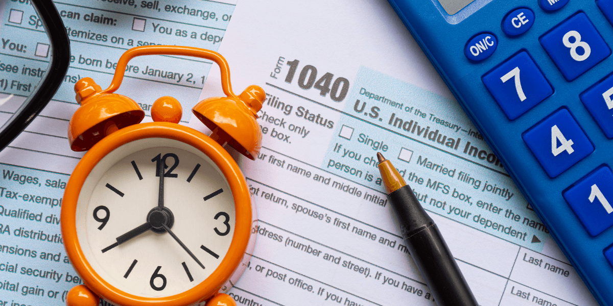 Tax form 1040 with a clock, calculator, and pen on a desk