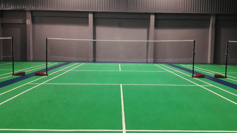 Indoor badminton court featuring green flooring and multiple nets set up