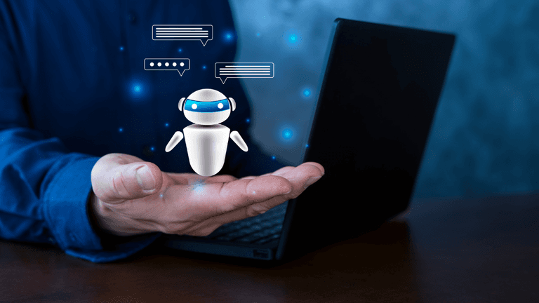 A person holding a small robot graphic above a laptop on a table