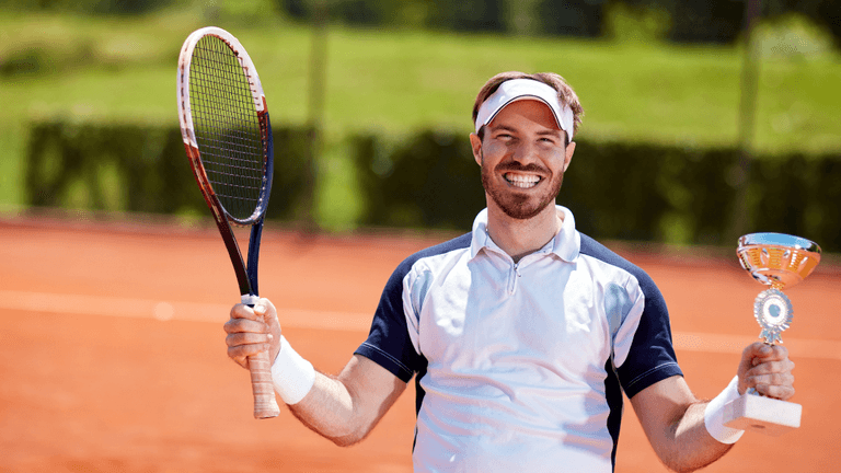 Smiling tennis player holding a trophy and racquet on a clay court