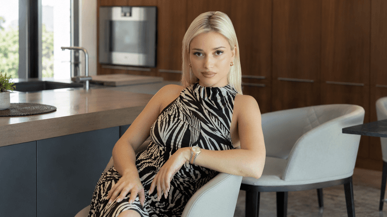 A seated woman with blonde hair poses in a stylish kitchen setting.