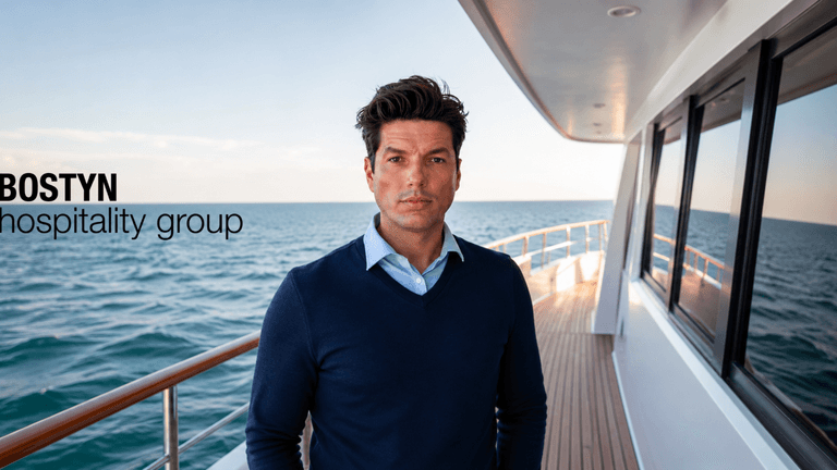 Man in a navy sweater stands on a yacht near the ocean