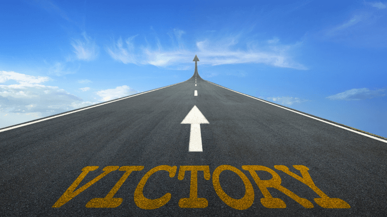 A road stretches upward with an arrow and the word "VICTORY" painted on the surface