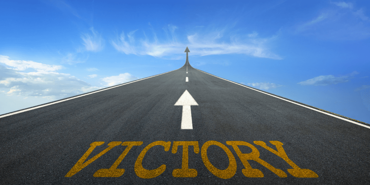 A road stretches upward with an arrow and the word "VICTORY" painted on the surface