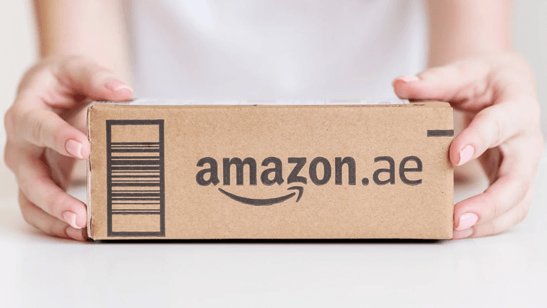 A person holding an Amazon package marked with the logo for Amazon.ae