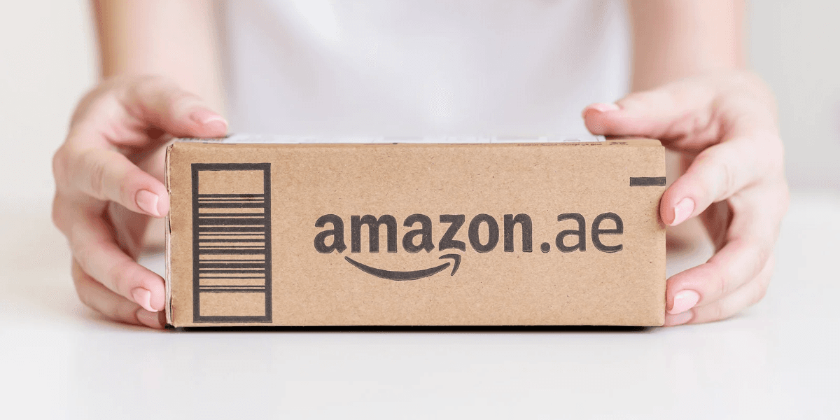 A person holding an Amazon package marked with the logo for Amazon.ae