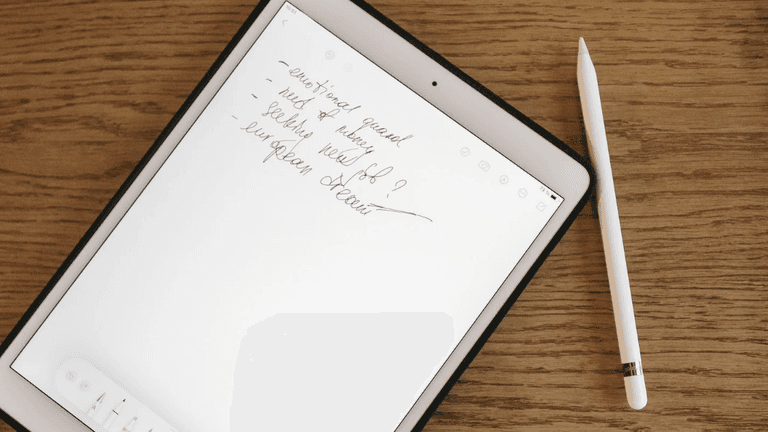 A tablet on a wooden surface displays handwritten notes beside a stylus.